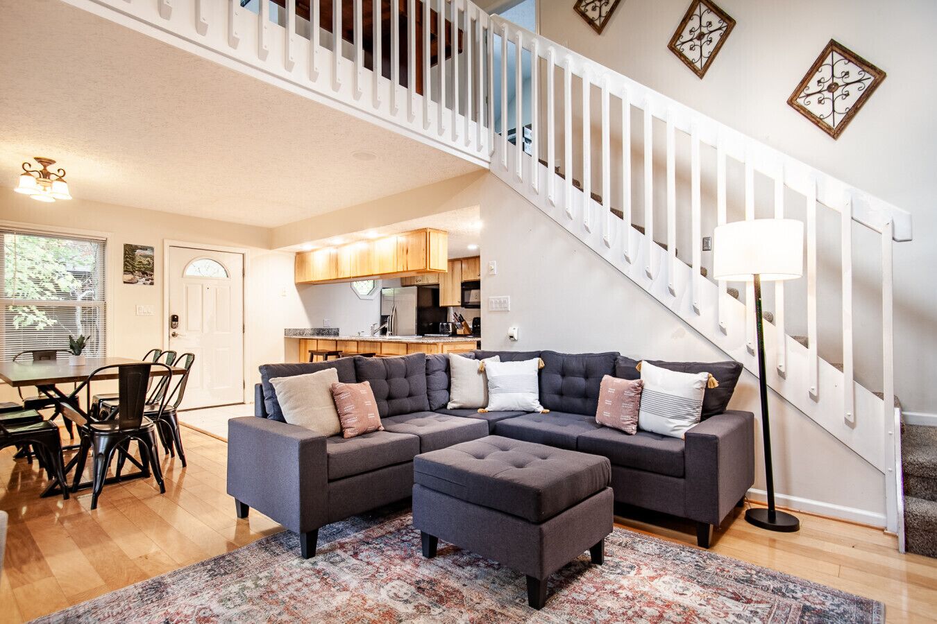 A modern living room with a sectional sofa, ottoman, and a staircase with a railing.