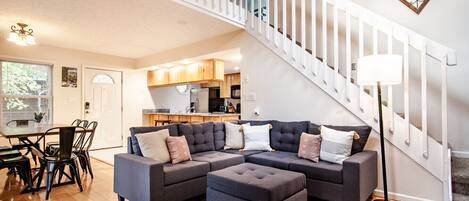 A modern living room with a sectional sofa, ottoman, and a staircase with a railing.