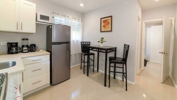 A compact kitchen with white cabinets, a stainless steel refrigerator, a microwave, and a coffee maker. There is a small dining table with two chairs and a potted plant. - Stylish 1-bedroom apartment in delightful Buckleys with WiFi, AC (Buckleys)