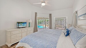 Ein Schlafzimmer mit einem Bett, einem Fernseher, einem Deckenventilator und Blick auf einen Außenpool.
