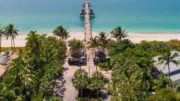 Ein Strandresort mit einer langen Pier, die sich ins Meer erstreckt, umgeben von Palmen und Strandhütten.