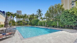 A rectangular swimming pool with a tiled deck, surrounded by palm trees and lounge chairs.