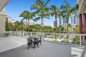 Varanda com mesa e cadeiras, vista para palmeiras e paisagem urbana.