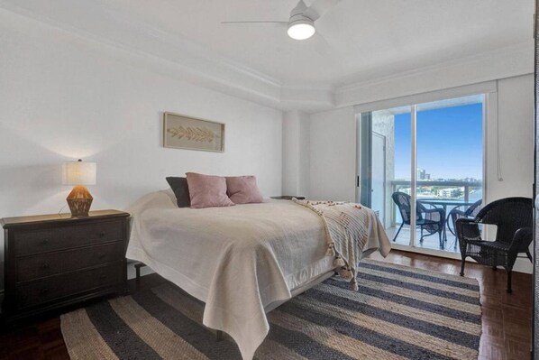 Une chambre à coucher comprenant un lit, une table de chevet, une lampe, une fenêtre donnant sur un beau paysage et un balcon avec des chaises.