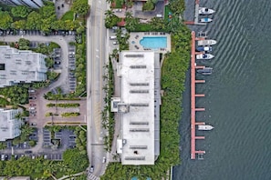 Vue aérienne d’un hôtel situé sur la côte, avec une piscine, un parking et des bateaux amarrés.