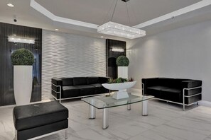 A modern living room with a glass coffee table, black sofas, and a large potted plant. - Le Petit Italie ,Water view 2/2 with pool (Sunny Isles Beach)