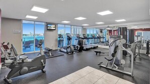 A gym with cardio machines, weight stations, and a large window with a city view.