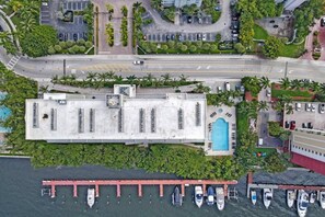 An aerial view of a hotel with a swimming pool, parking area, and boats docked at a pier. - Le Petit Italie ,Water view 2/2 with pool (Sunny Isles Beach)