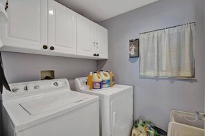 A laundry room with a washer and dryer, a window with curtains, and detergent bottles on the counter. - Le Petit Italie ,Water view 2/2 with pool (Sunny Isles Beach)