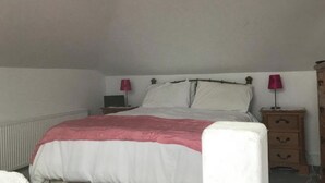 En säng med en vit och rosa sängkappa, två sängbord med lampor och ett träbord med lådor.