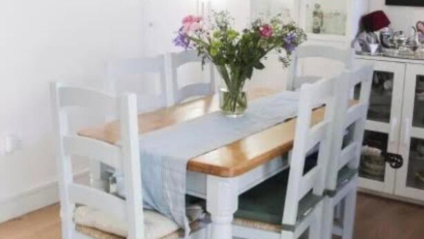Ett matbord med en vas med blommor, omgivet av vita stolar.
