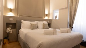 A neatly made bed with pillows and towels, a bedside table, and a vase with flowers. - Superior Double Room with AC (Roma)
