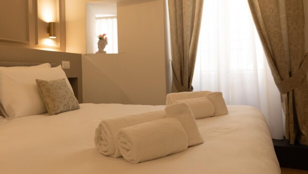 A neatly made bed with rolled towels, a bedside lamp, and a window with curtains. - Superior Double Room with AC (Roma)