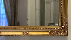 A mirror with an ornate gold frame, a chandelier, and a marble wall. - De Vince Suites   Luxury Rooms   King Executive (Roma)
