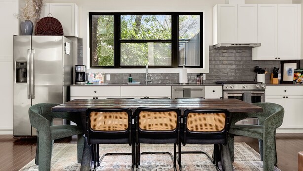 A modern kitchen with white cabinets, a large window, a dining table with four chairs, and a built-in stove. - Stylish Pearl District Stay - Relax, Dine & Explore (San Antonio)