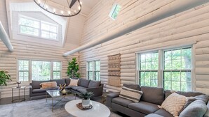 Ein rustikales Holzhäuschen im Inneren zeigt ein Wohnzimmer mit einem grauen Sofa, einem Couchtisch und einem großen Fenster.
