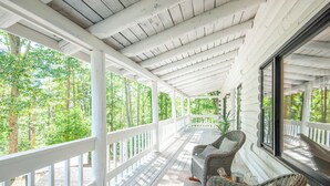 Eine überdachte Veranda mit Korbmöbeln und Blick auf einen Wald.