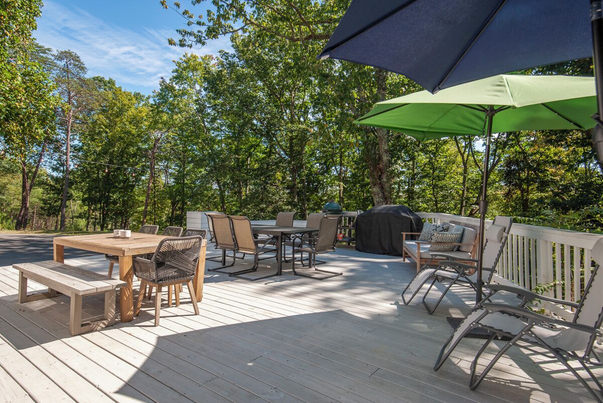 Una terraza de madera con mobiliario exterior, incluyendo una mesa, sillas y una parrilla.