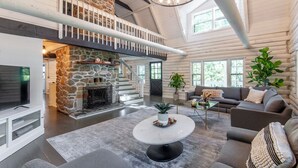 Ein großzügiges Blockhaus-Interieur mit Kamin aus Stein, einem Balkon und einer modernen Wohnbereitschaft mit Sofas und Couchtisch.