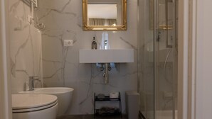 A bathroom with a white sink, two toilets, a mirror, and a shower. - De Vince Suites   Luxury Rooms   Roma Termini   King De Luxe (Roma)