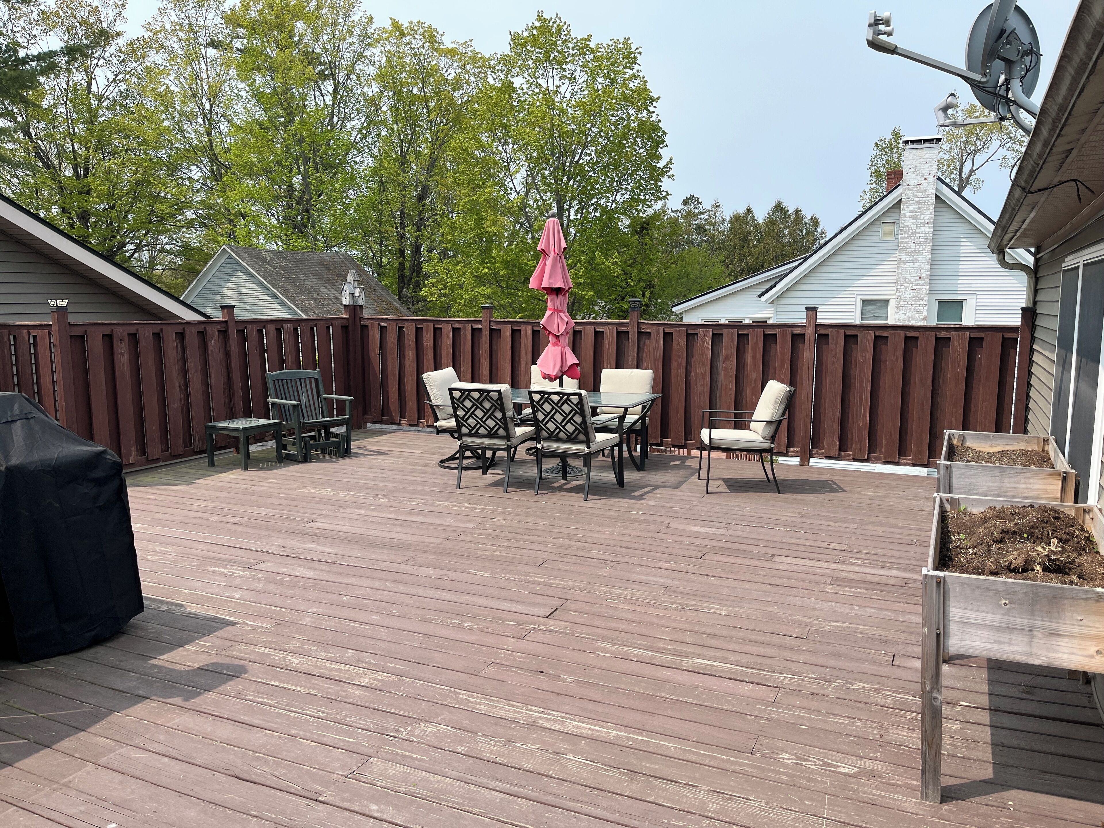 Eine Holzterrasse mit Gartenmöbeln, darunter Stühle und ein Tisch, umgeben von einem Holzzaun.