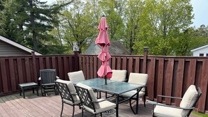 Une terrasse dotée d’une table avec un plateau en verre et de quatre chaises, d’une petite table et d’un banc.