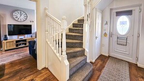 A staircase with a carpeted landing and a white railing, leading to a door with a window. A flat-screen TV is mounted on the wall above the staircase. - Boughton 3 Bed Semi by Fortuna Property Portfolio (Gloucester)