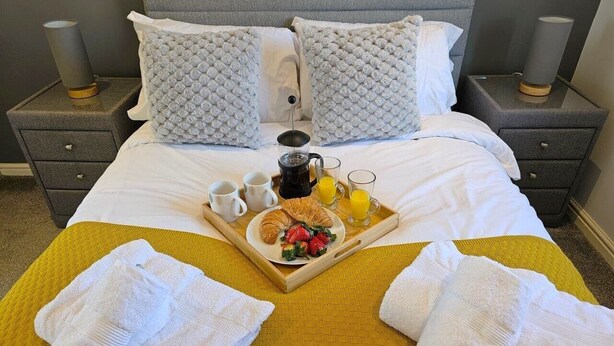 A neatly made bed with a tray of breakfast items, including croissants, strawberries, and juice, on a yellow bedspread. - Boughton 3 Bed Semi by Fortuna Property Portfolio (Gloucester)