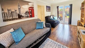 A living room with a sofa, armchairs, and a large cityscape painting. - Boughton 3 Bed Semi by Fortuna Property Portfolio (Gloucester)