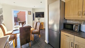A compact kitchen with a built-in microwave, a refrigerator, and wooden cabinets. - Boughton 3 Bed Semi by Fortuna Property Portfolio (Gloucester)