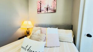 Een net opgemaakt bed met een kussen waarop 'zoete dromen' staat en een schilderij van de Eiffeltoren aan de muur.