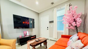 Een woonkamer met een flatscreen televisie, een bank, een salontafel en een decoratieve roze boom.