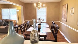 A dining room with a long table, chairs, a chandelier, and a vase with white pebbles.
