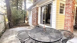 A patio with a round metal table and chairs, a brick chimney, and a sliding glass door leading to a covered area.