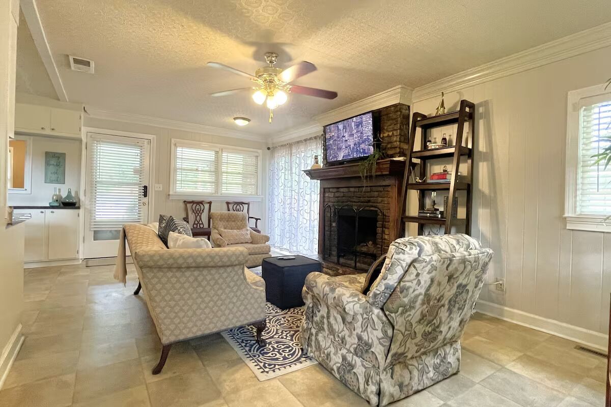 A living room with a fireplace, two patterned armchairs, a coffee table, and a television.