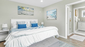 Une chambre à coucher avec un grand lit, deux tables de chevet, une commode et une salle de bain visible à travers une porte ouverte.