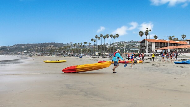 Une plage avec des kayaks et des gens, des palmiers et des bâtiments en arrière-plan.
