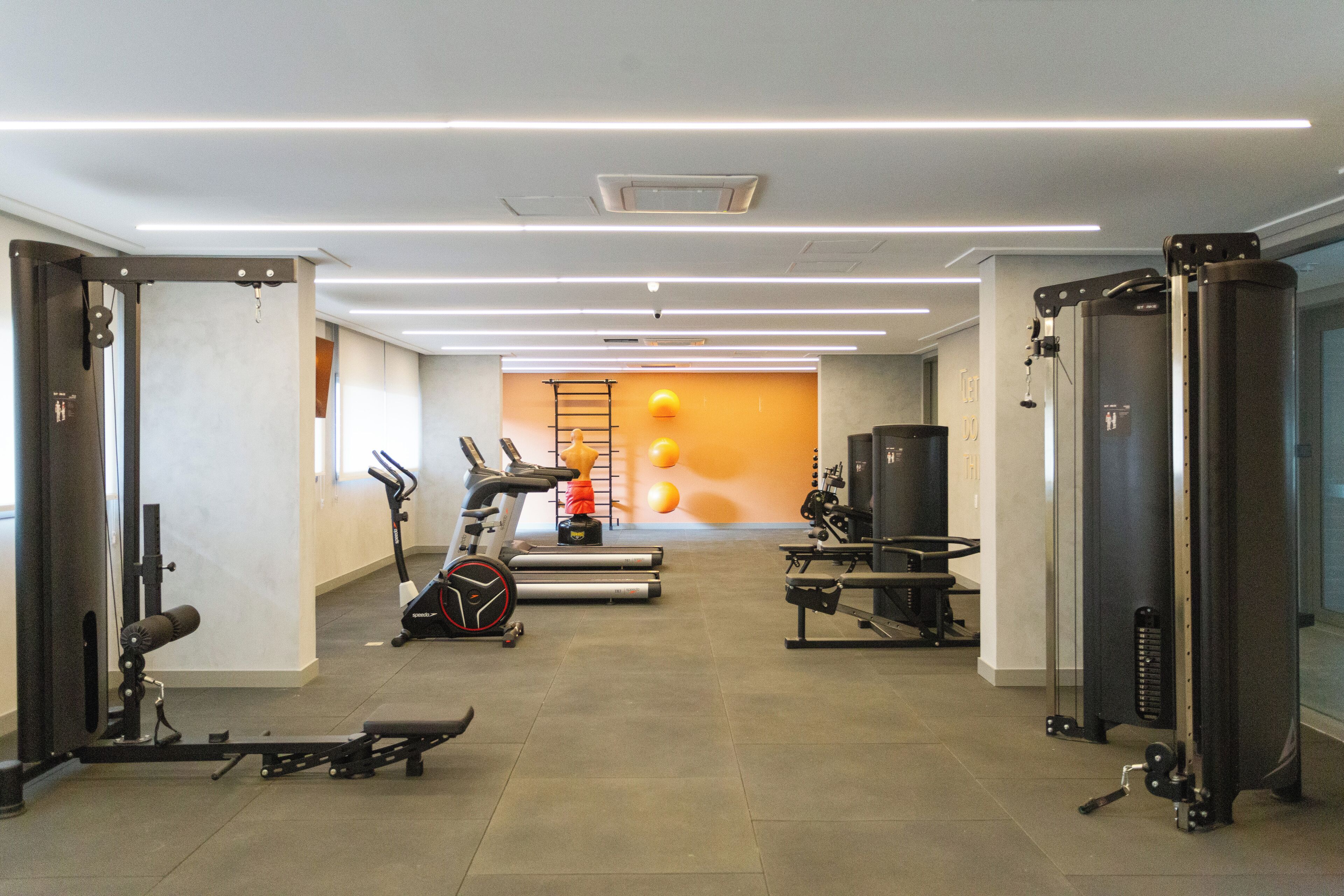 A modern gym with treadmills, weight machines, and a wall with orange exercise balls.