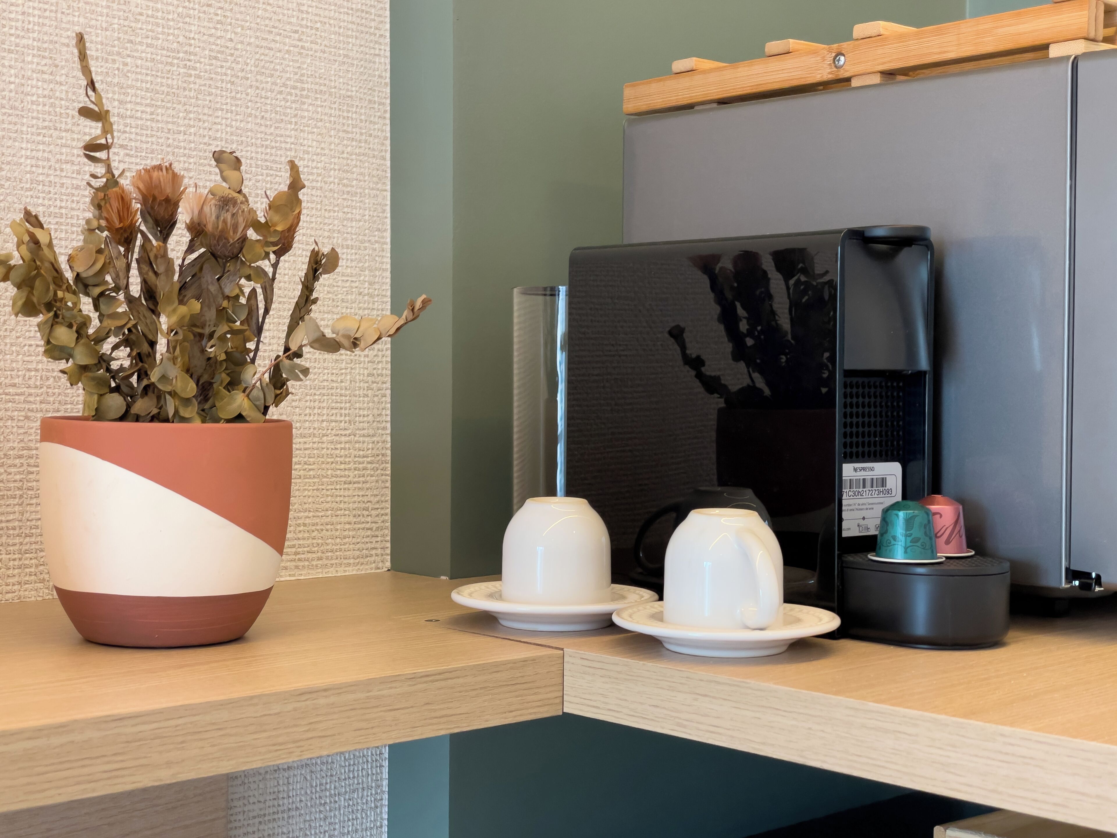 A coffee machine, a potted plant, and two cups on a wooden counter.