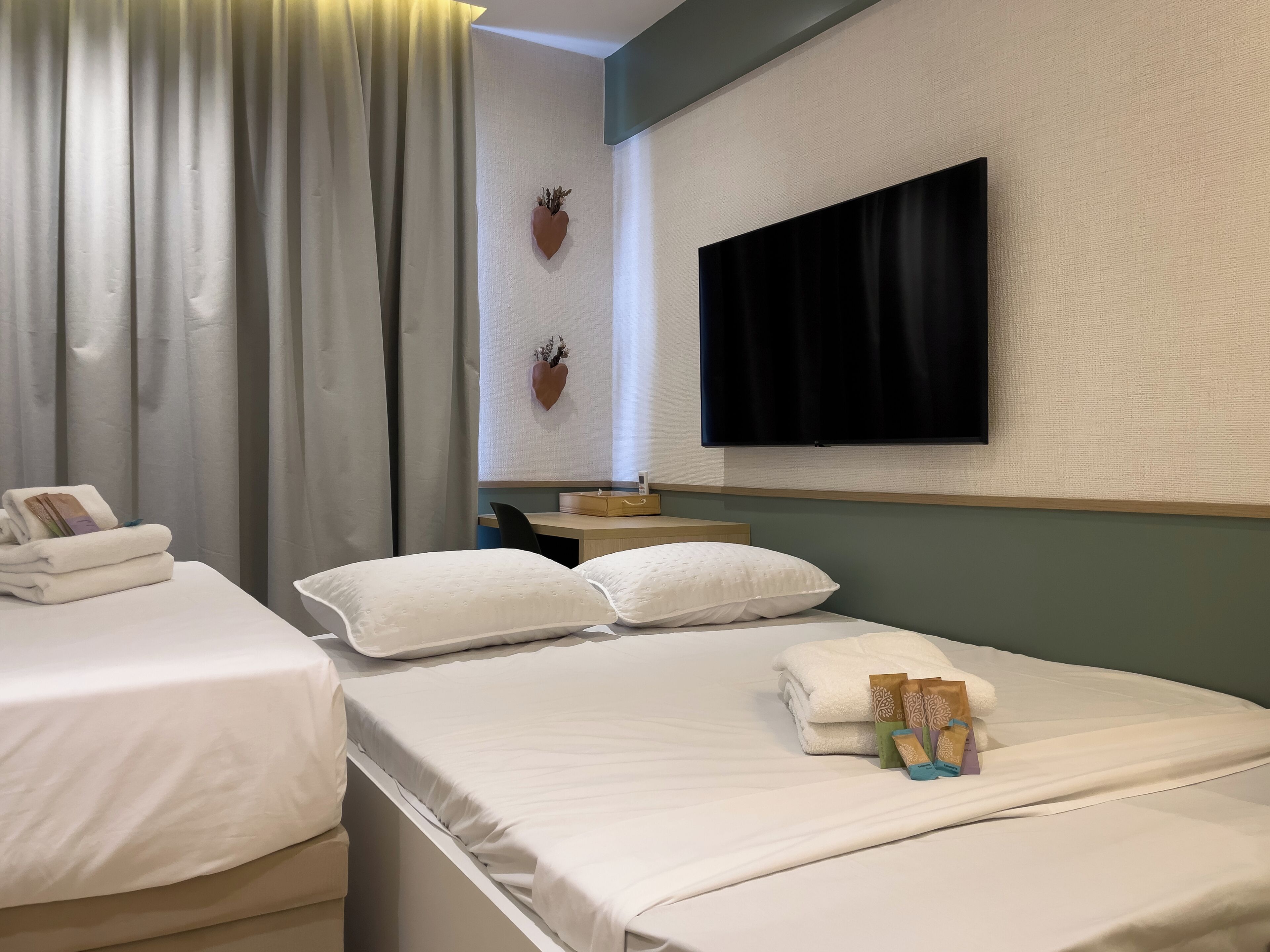 Una camera d'albergo con due letti, una TV a schermo piatto fissata al muro e una piccola scrivania con una sedia.