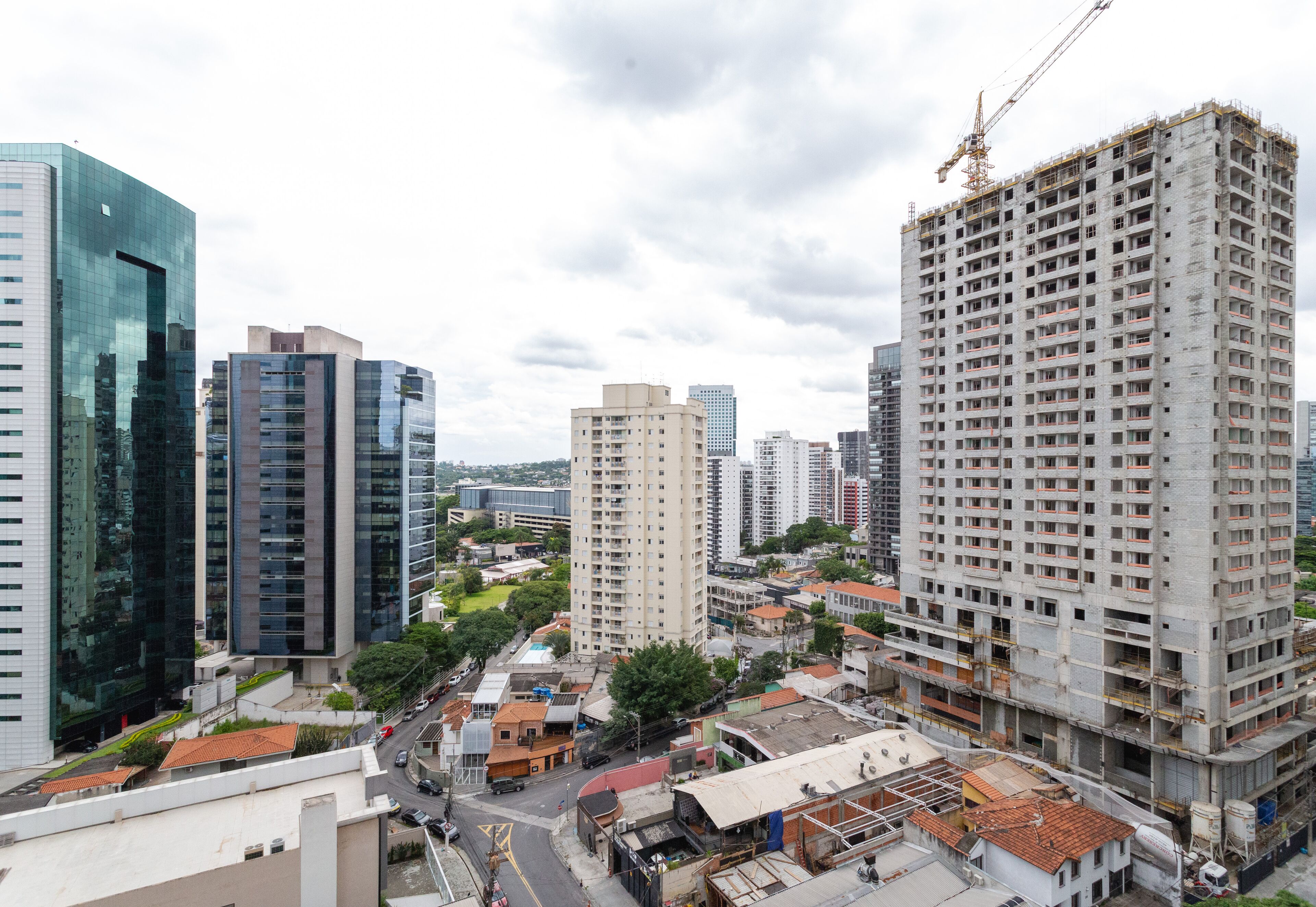 A high-rise building with a construction crane, surrounded by other tall buildings and a busy street.