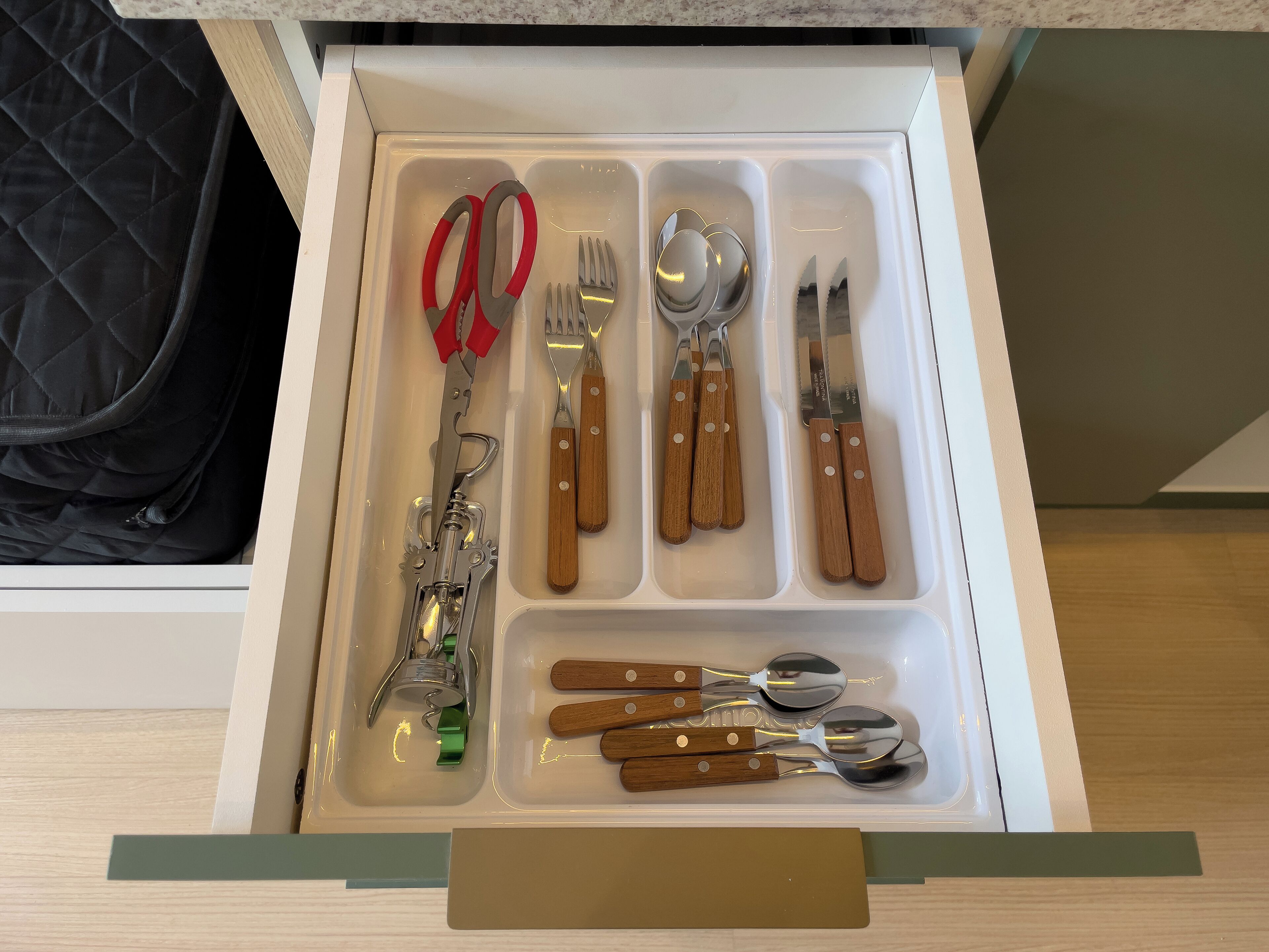 A drawer with various utensils including scissors, forks, spoons, and a can opener.