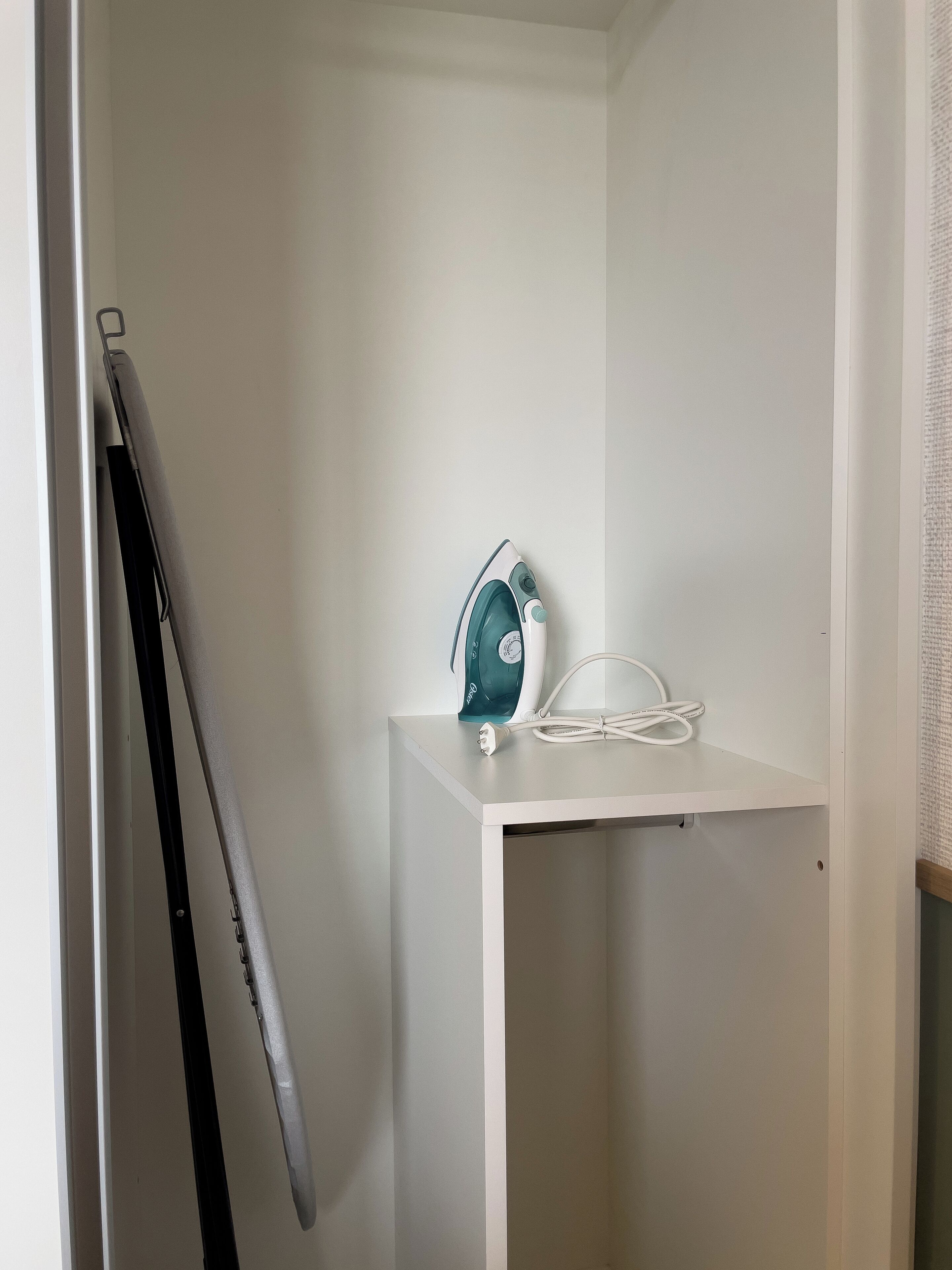 A white shelf with a teal iron and a white power cord.