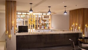 Et moderne køkken med en central ø, hængende lamper og en bar med glas og flasker.
