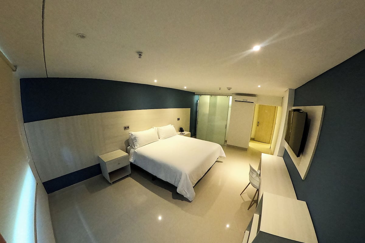 A modern hotel room with a large bed, bedside tables, a desk, and a flat-screen TV mounted on the wall.