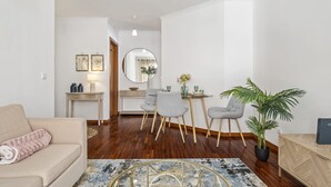 A modern living room with a beige sofa, a dining area with a round table and chairs, a mirror, and a potted plant. - Locally by Homie in Funchal (Funchal)