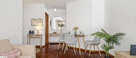 Ett modernt vardagsrum med en beige soffa, en matplats med ett runt bord och stolar, en spegel och en krukväxt.