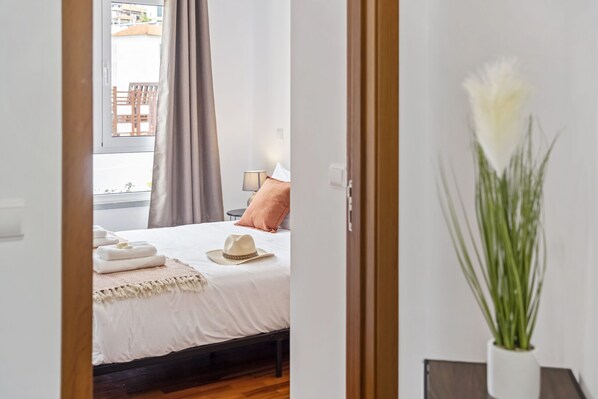 Un dormitorio con cama, mesita de noche, lámpara, ventana con cortinas y una planta en maceta.