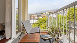 A balcony with a chair, a small table with a book, and a potted plant. - Locally by Homie in Funchal (Funchal)