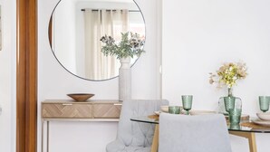 A dining area with a round mirror, a vase with flowers, and a table set with green glassware. - Locally by Homie in Funchal (Funchal)